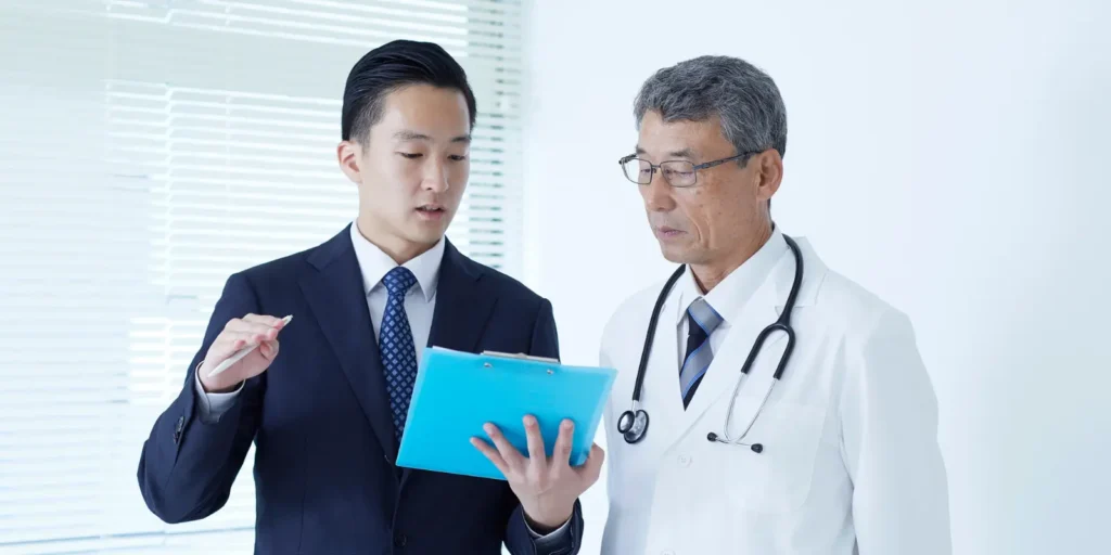 Doctor and hospital executive reviewing patient data on tablet during healthcare consultation and medical management meeting