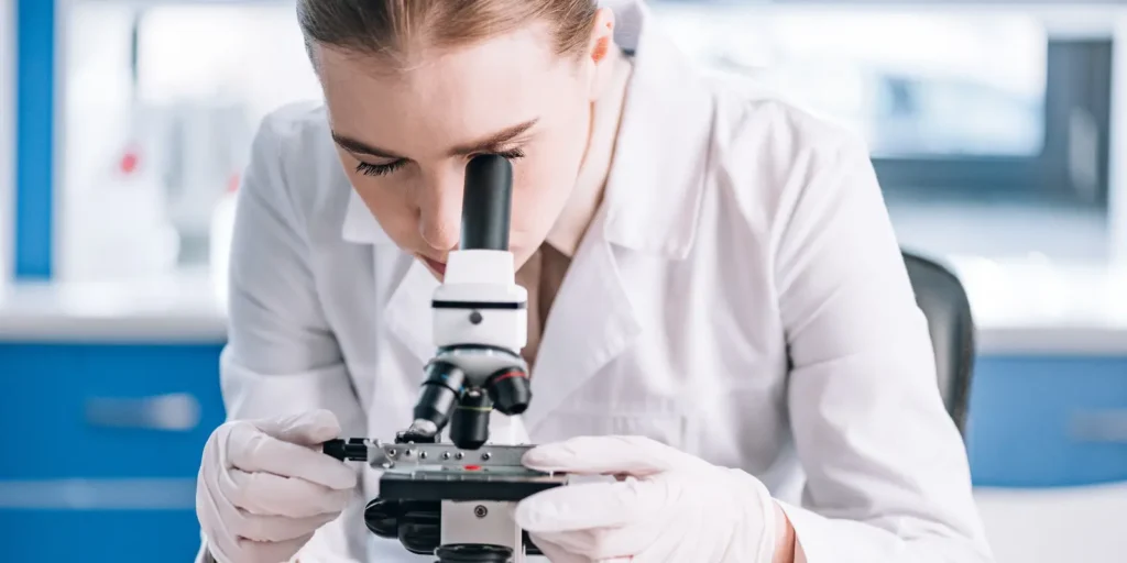 Scientist examining samples under a microscope for immunologist database research.